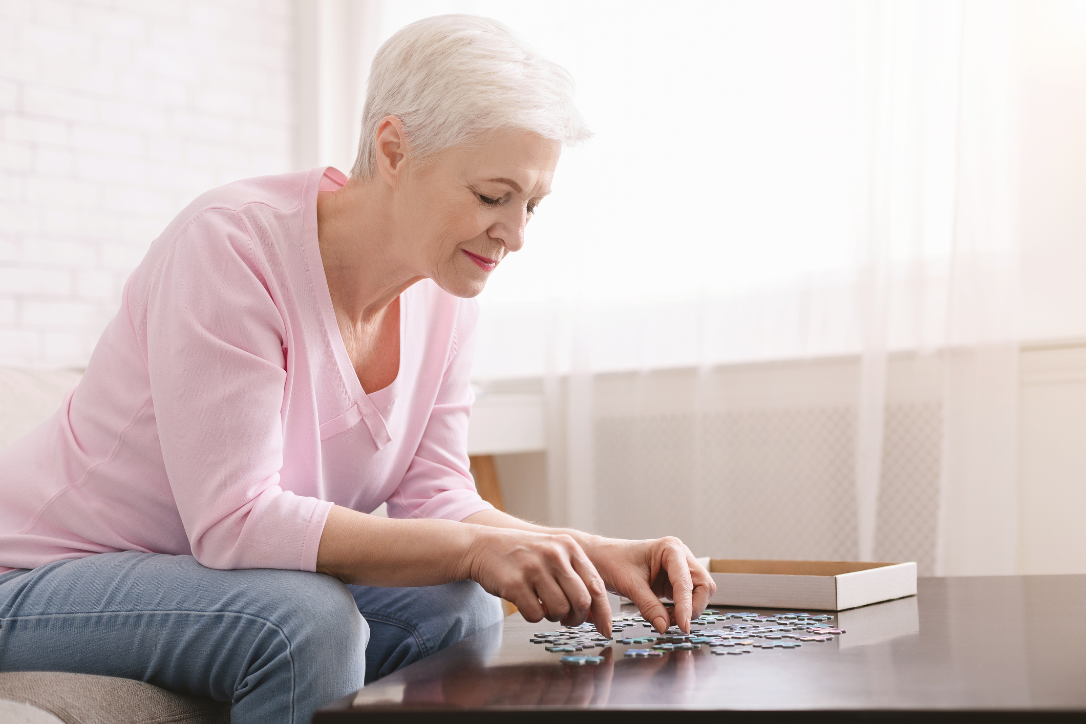 An elderly woman playing with a jigsaw puzzle, one of the best memory games for seniors to stay sharp.