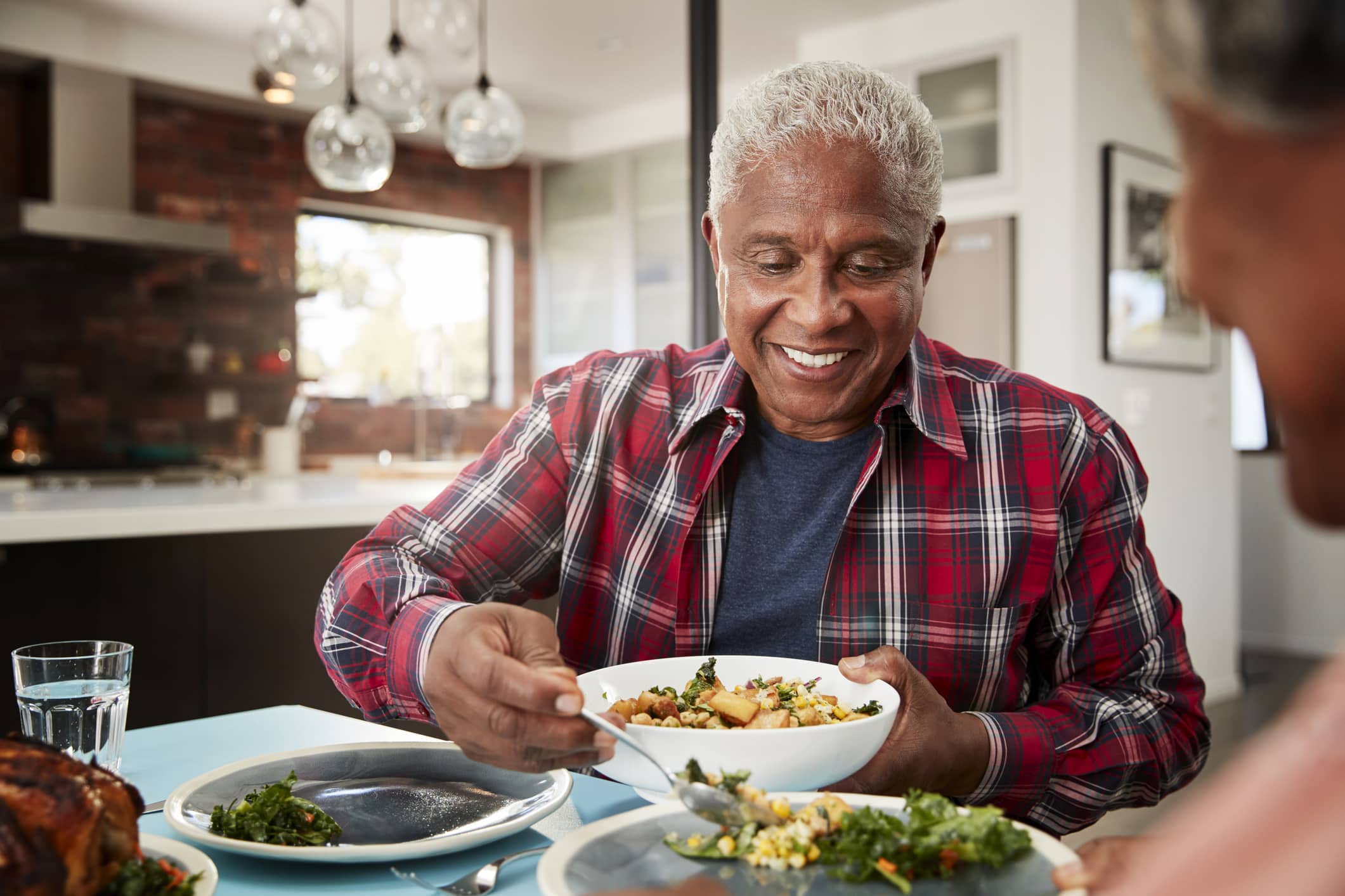 An older man serving food to his partner at the dinner table after learning about healthy eating tips for seniors.