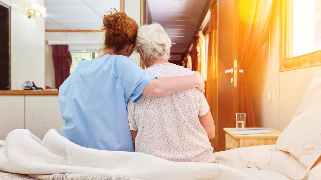 Nurse in hospice hugs elderly woman on bed for comfort while grieving